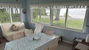 Ein Zimmer mit Esstisch, Stühlen, einer Couch und großen Fenstern mit Vorhängen.