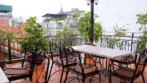 A terrace with a table and chairs, potted plants, and a view of buildings. - Hanoi Sunflower Westlake Homestay (Hanoi)