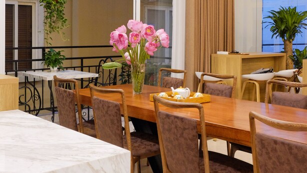 A modern dining area with a marble table, wooden chairs, and a vase of pink flowers. - Hanoi Sunflower Westlake Homestay (Hanoi)