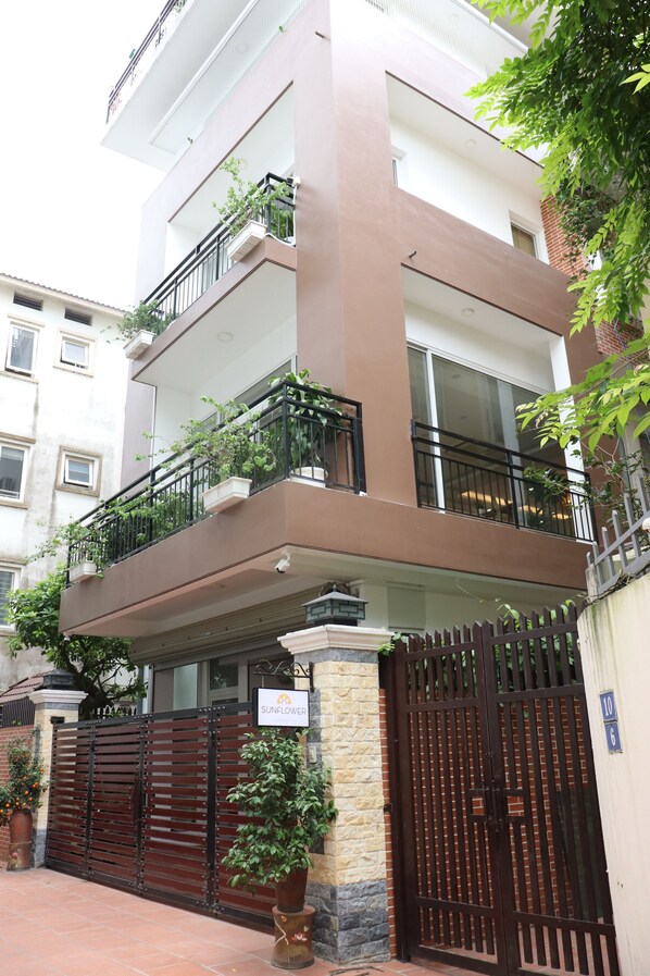 A multi-story residential building with balconies, a gated entrance, and potted plants.