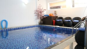 A swimming pool with a blue mosaic tile border, surrounded by wicker chairs with blue cushions, a small table with a vase of pink flowers, and a blue hose on the left. - Hanoi Sunflower Westlake Homestay (Hanoi)