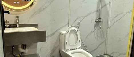 A bathroom with a toilet, a sink, a mirror, and a shower.