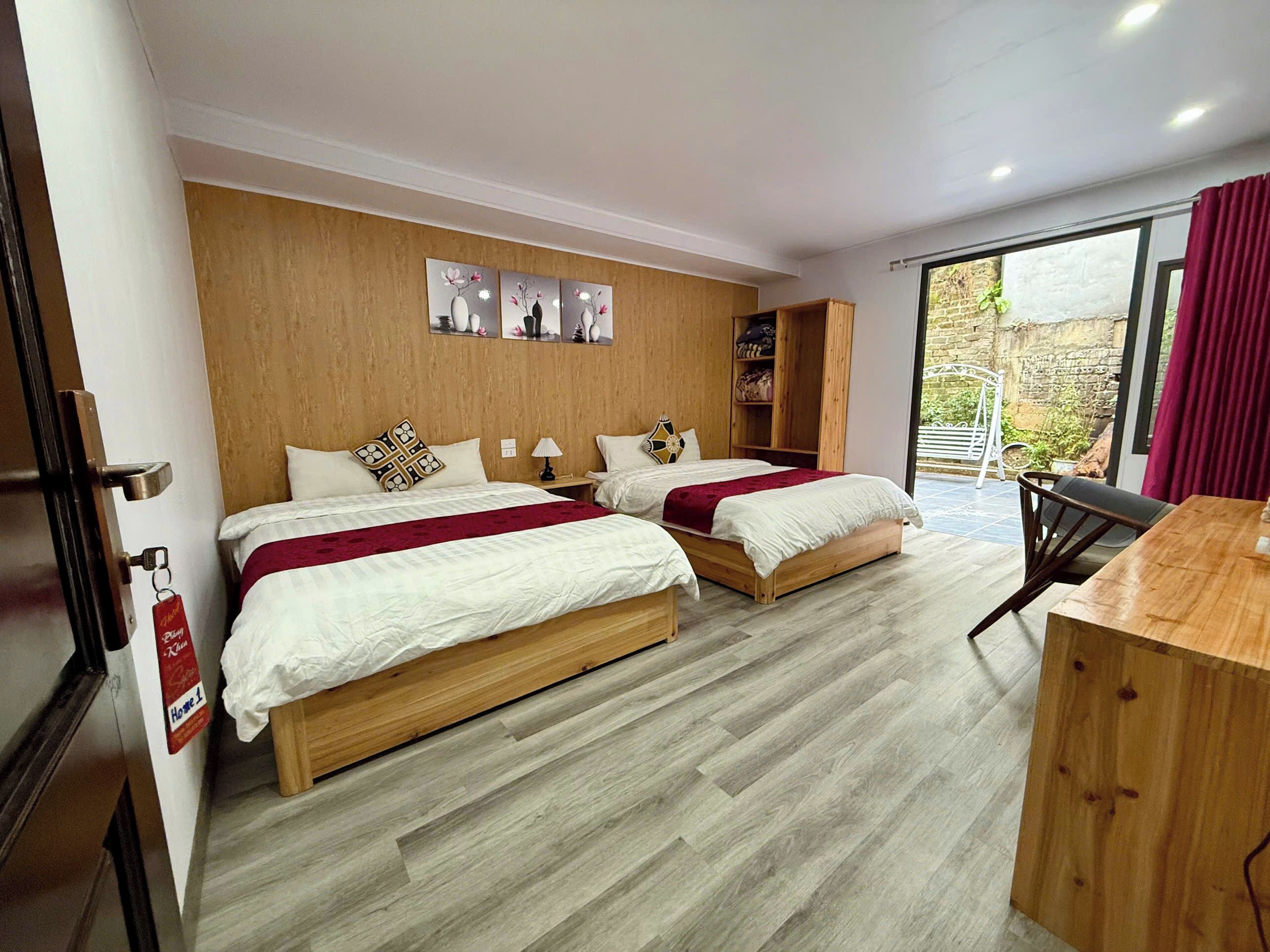 A hotel room with two beds, a wooden wardrobe, a desk, and a balcony with a view.
