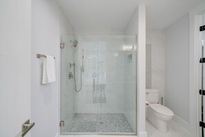 A modern bathroom with a glass-enclosed shower, a toilet, and a white tiled floor.