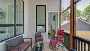 Eine überdachte Veranda mit Korbmöbeln, einem Glastisch und Blick in ein Schlafzimmer.