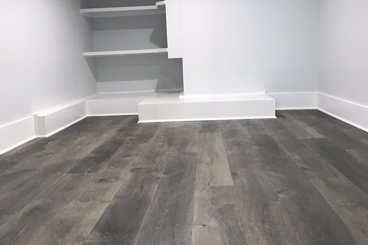 Una habitación con suelo de madera oscura, paredes blancas y una escalera que sube a un nivel superior.