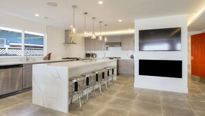 Une cuisine moderne dotée d’un grand îlot central, d’appareils électroménagers en acier inoxydable et de luminaires suspendus.