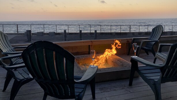 Une terrasse avec des sièges extérieurs et un foyer, donnant sur une étendue d’eau.