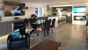 Une cuisine moderne dotée d’un îlot central, un coin repas avec une table en verre et un espace de vie avec un canapé en cuir.