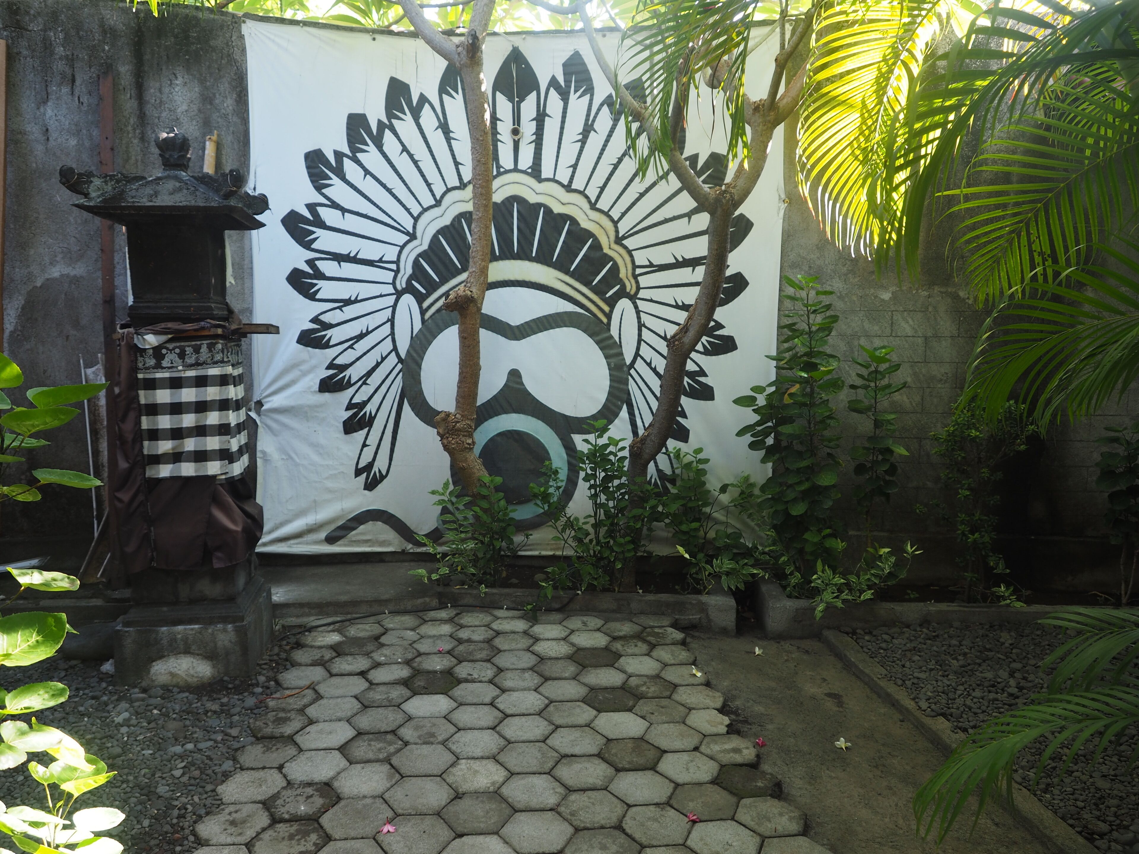 A courtyard with a hexagonal tiled floor, a large mural on a wall, and a small tree.