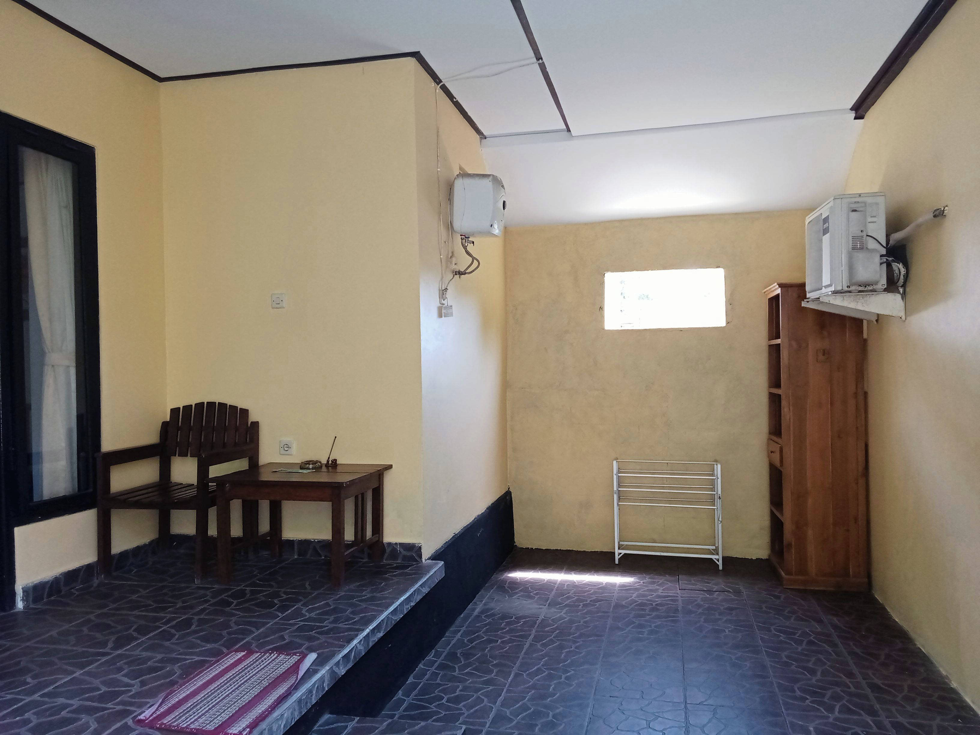 Una habitación pequeña con un banco de madera, una mesa, un perchero metálico y una ventana.