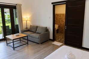 A room with a sofa, a small table, a bed, and a sliding door leading to a bathroom. - Scuba Tribe Bali dive-resort (Tulamben)