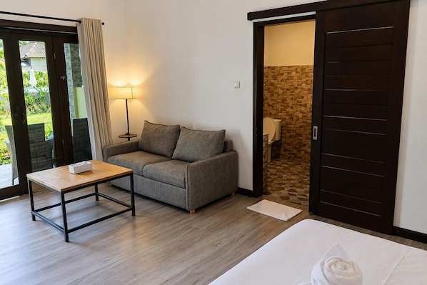 A room with a sofa, a small table, a bed, and a sliding door leading to a bathroom. - Scuba Tribe Bali dive-resort (Tulamben)