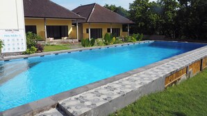 Piscina com degraus revestidos, rodeada por um espaço gramado e um edifício com telhado telhado.