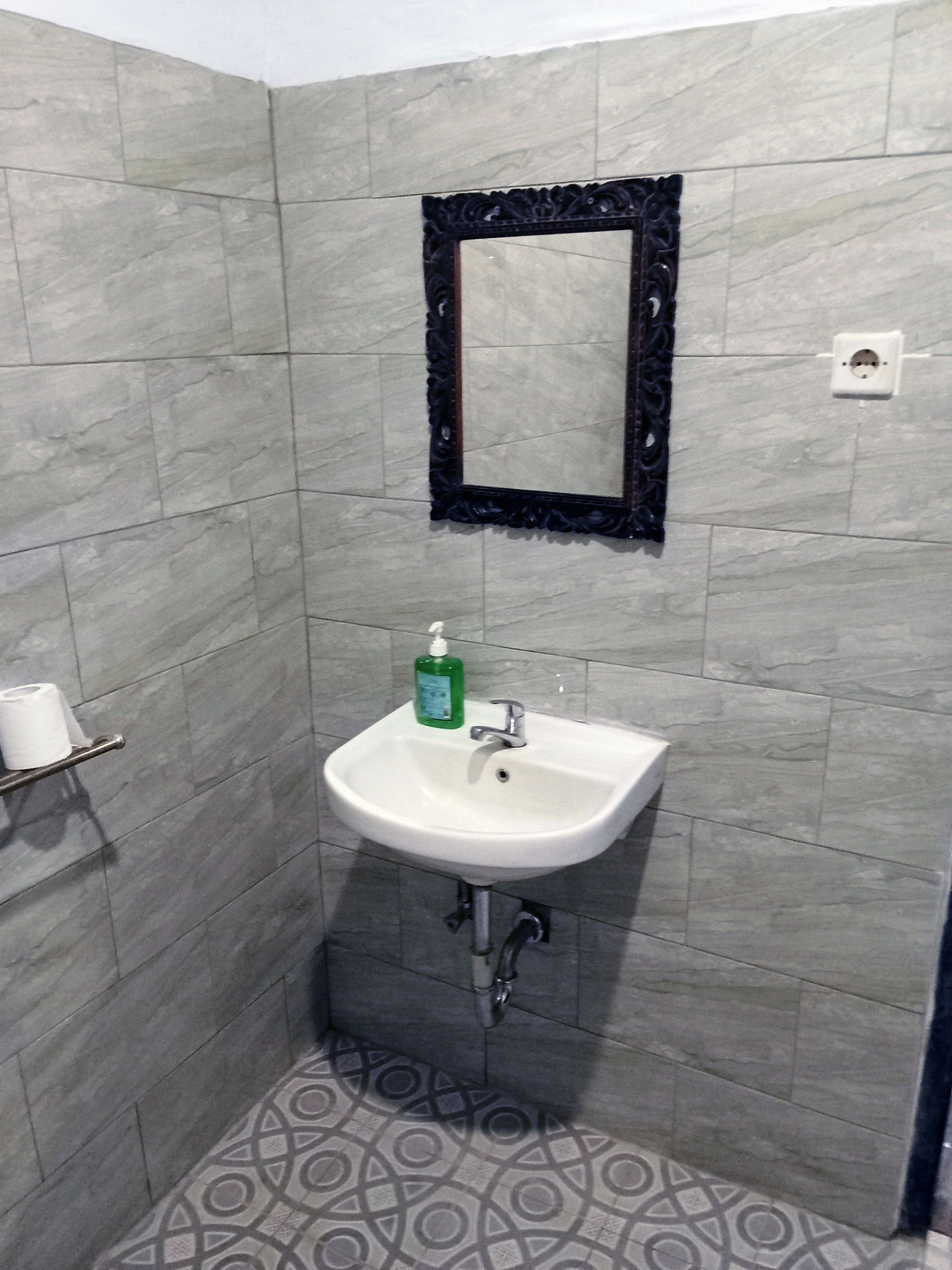 A bathroom with a white sink, a mirror with a dark frame, and patterned floor tiles.