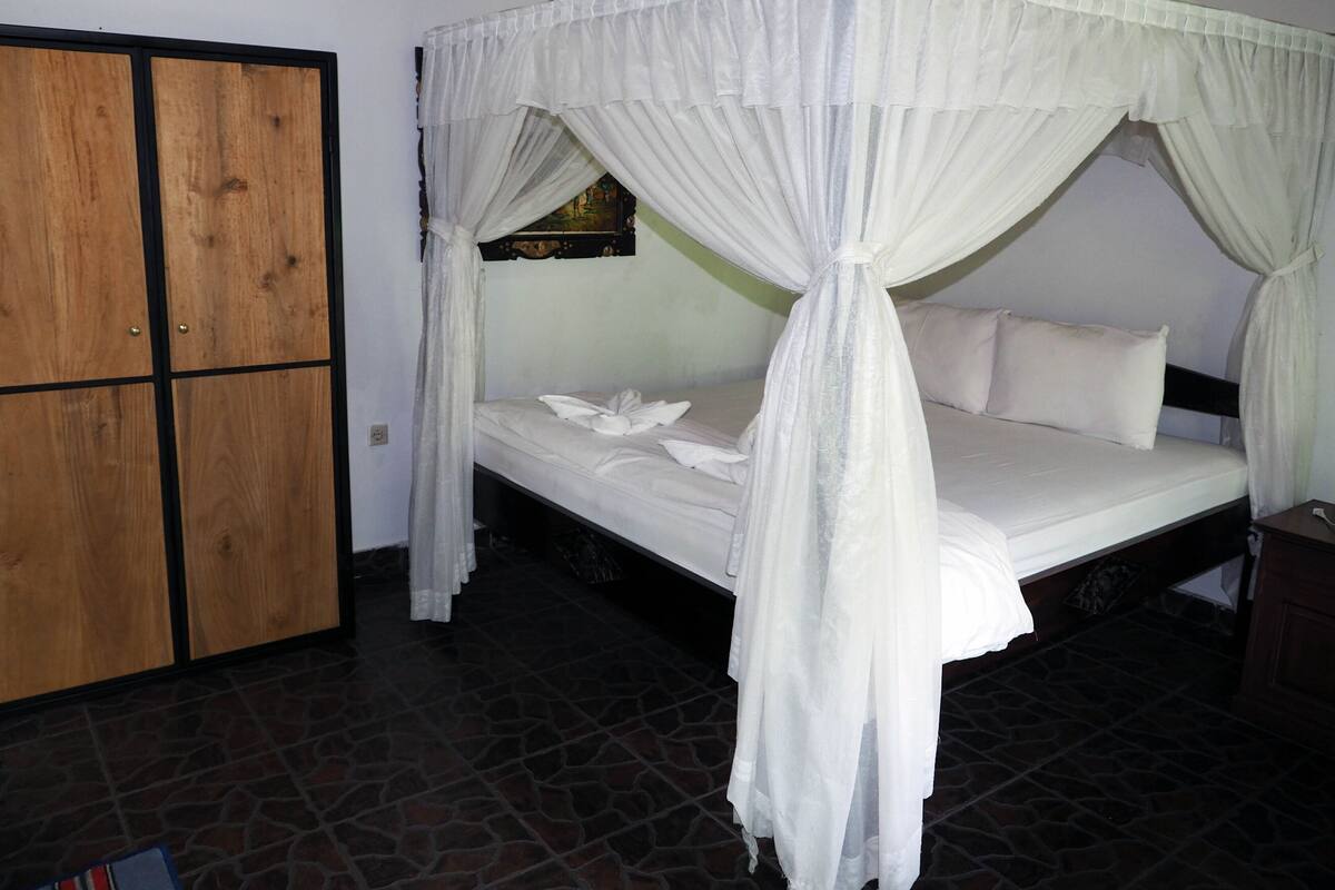 A room with a bed under a canopy, a wooden wardrobe, and a tiled floor.