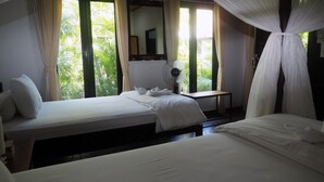 Quarto com duas camas, uma mesa, um ventilador e uma janela com cortinas.