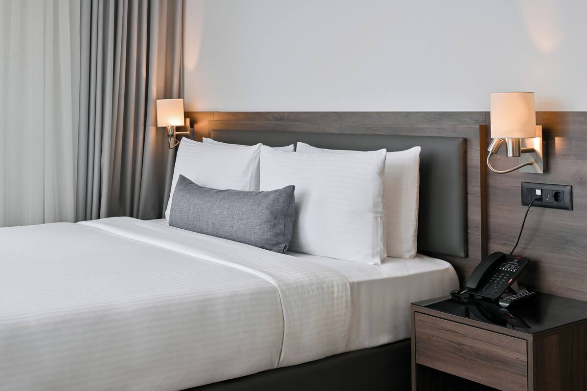 Ein Hotelzimmer mit Bett, Nachttischlampen, einem Telefon auf dem Nachttisch und einer Steckdose.