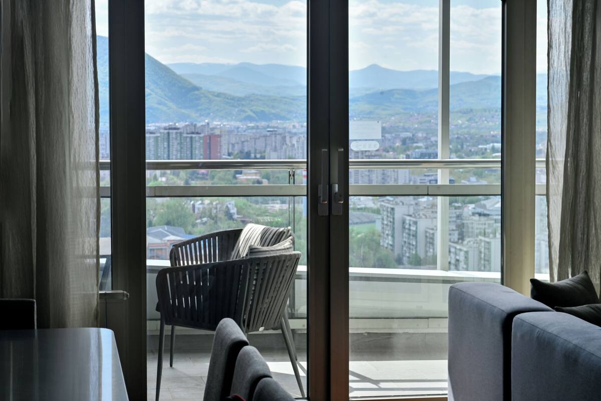 Ein stilvolles Wohnzimmer mit großem Fenster, einer Couch, einem Sessel und einem Tisch.