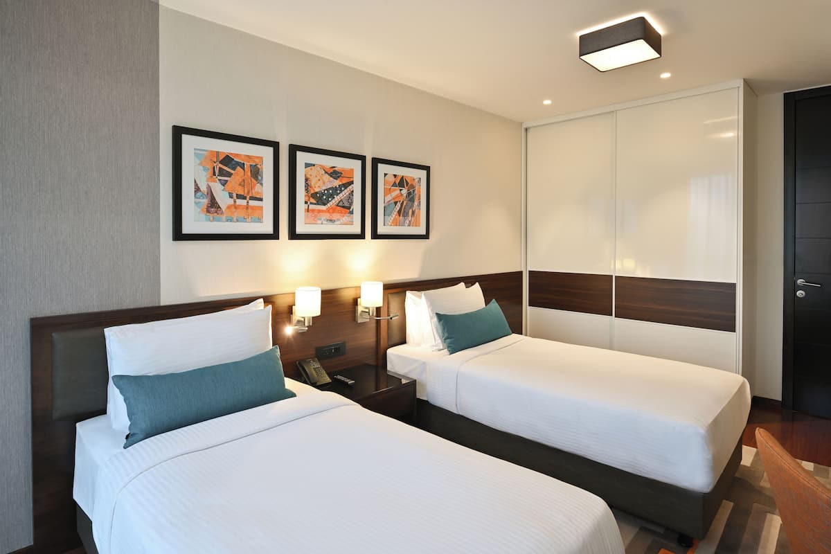 Ein Hotelzimmer mit zwei Betten, einem Nachttisch, einem Telefon, Wandleuchten und drei gerahmten Bildern.