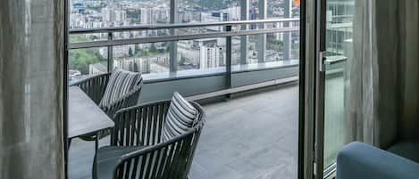 A balcony with a view of a cityscape, a table, and two chairs.
