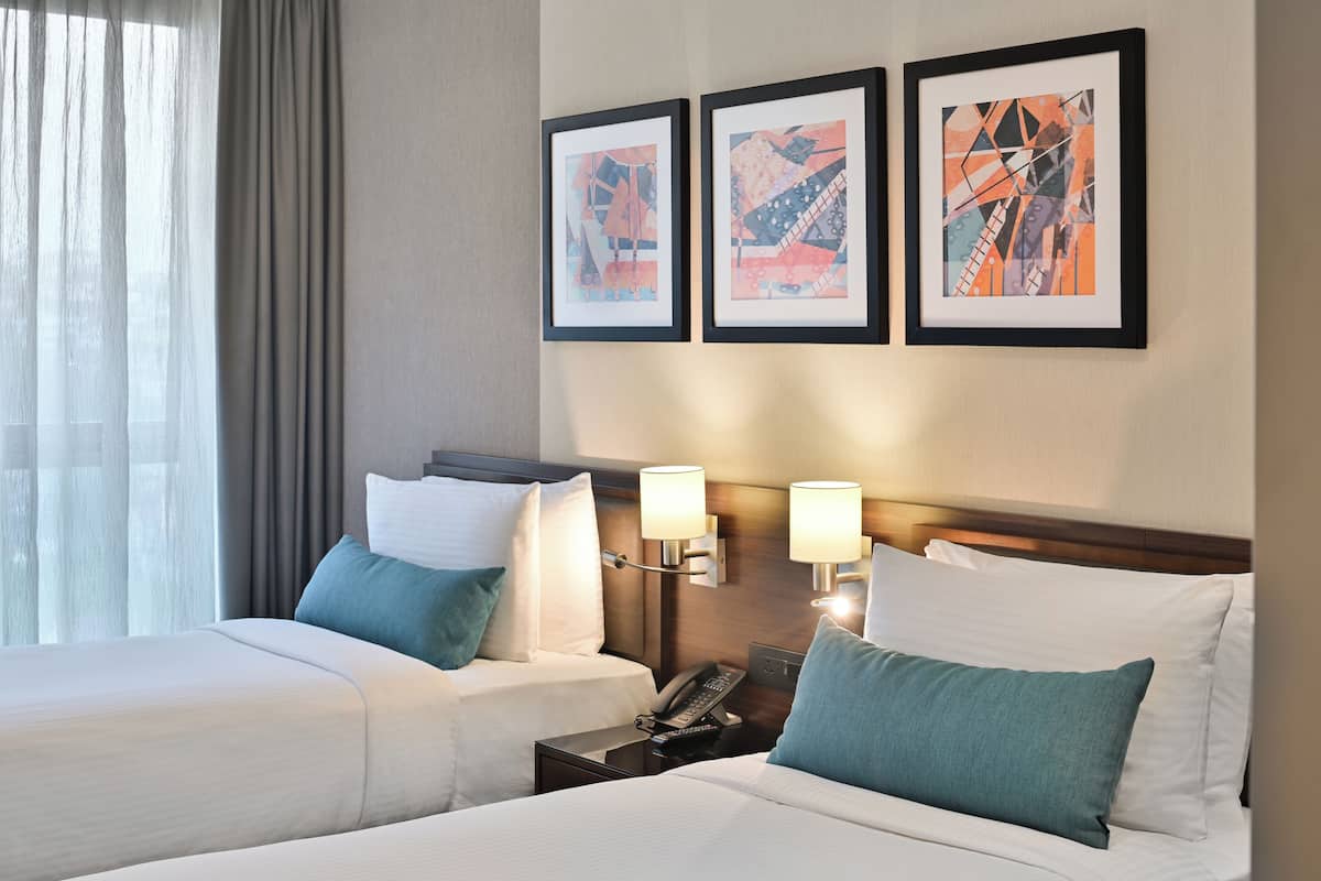 Ein Hotelzimmer mit zwei Betten, einem Nachttisch mit Telefon, Wandlampen und einem abstrakten Kunstwerk an der Wand.