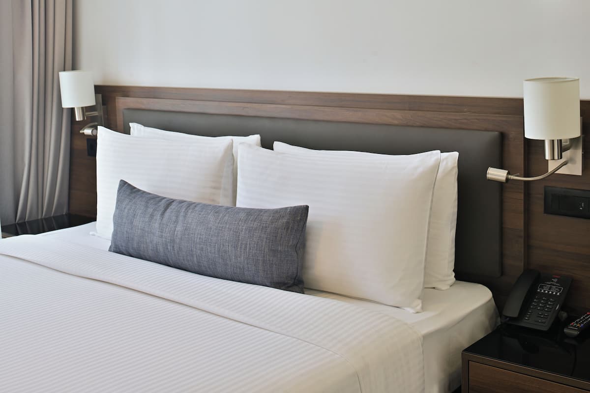 Ein Hotelzimmer mit einem Bett, Kissen, einem Nachttisch mit Telefon und Wandlampen.
