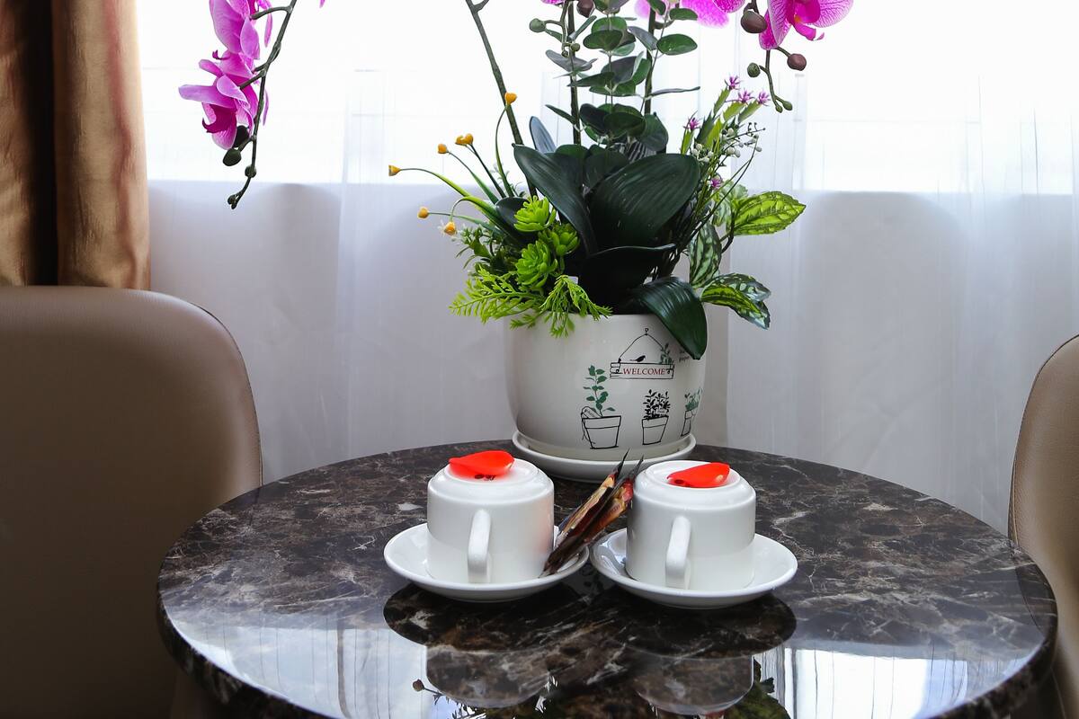 A round table with two white cups and a vase of pink orchids.