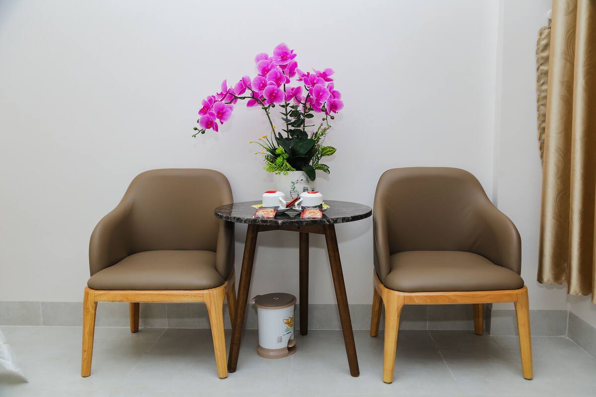 A room with two brown leather chairs, a small round table with a vase of pink flowers, and a trash bin.