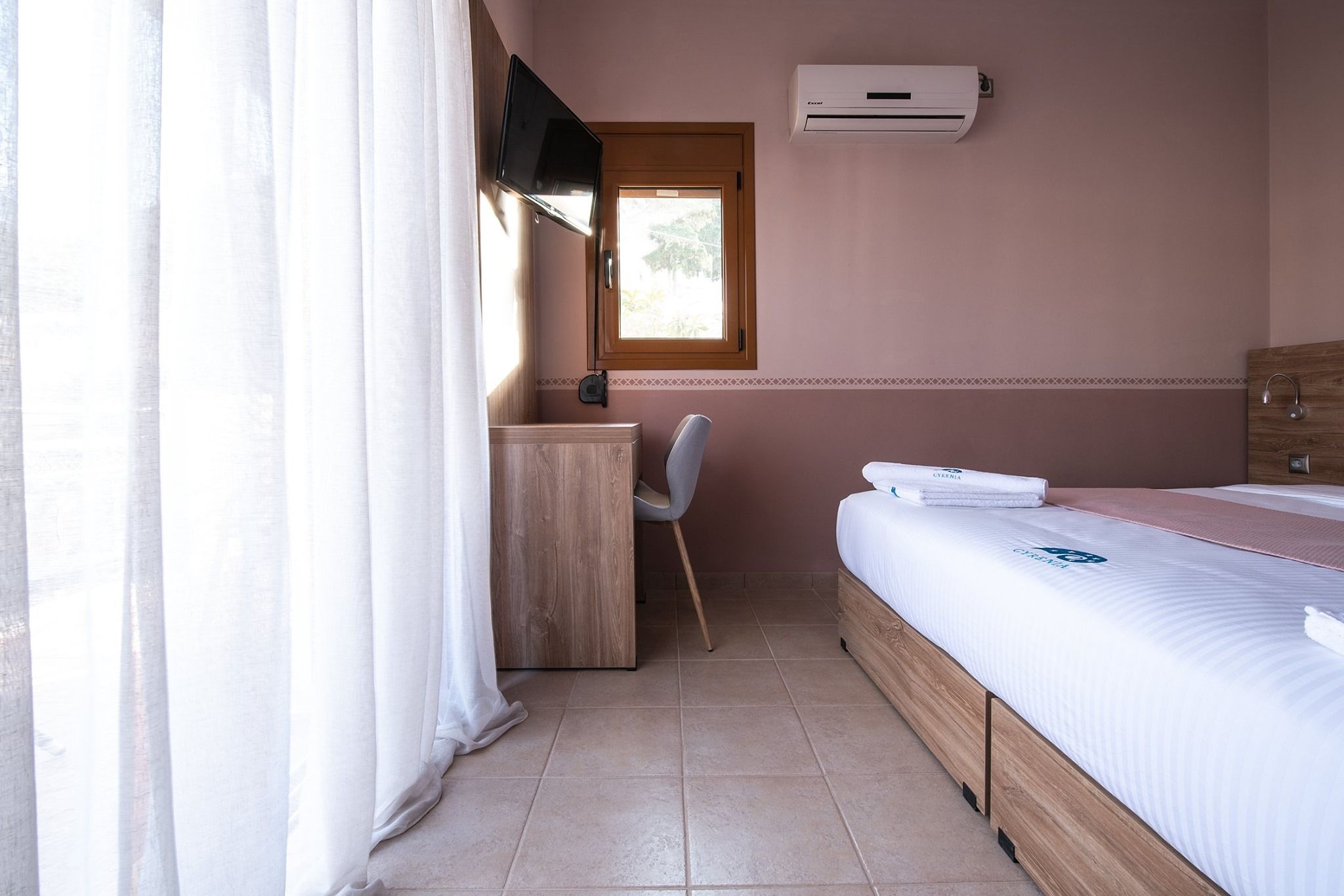 Quarto com cama, escrivaninha, cadeira, janela e ar condicionado.
