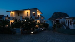 Una casa de dos pisos con un balcón, una montaña al fondo y un camino de entrada de grava.