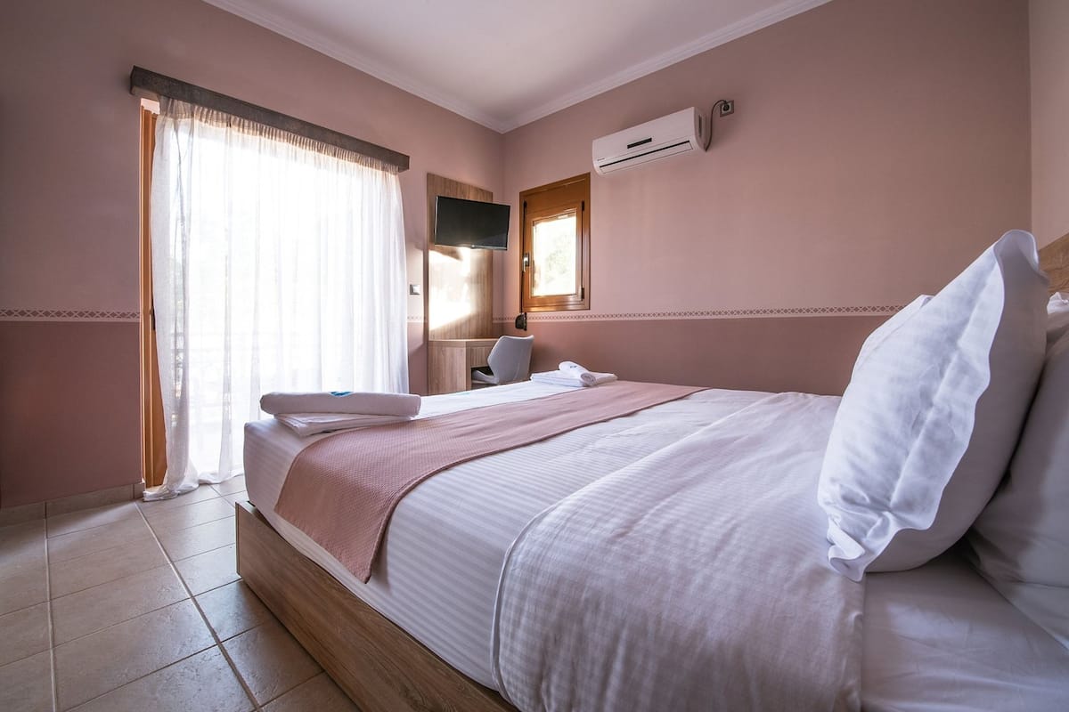 A hotel room with a bed, a TV mounted on the wall, and an air conditioning unit.