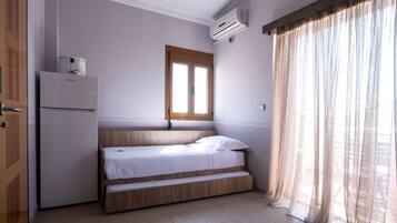 Una habitación pequeña con cama, ventana, puerta y aire acondicionado.