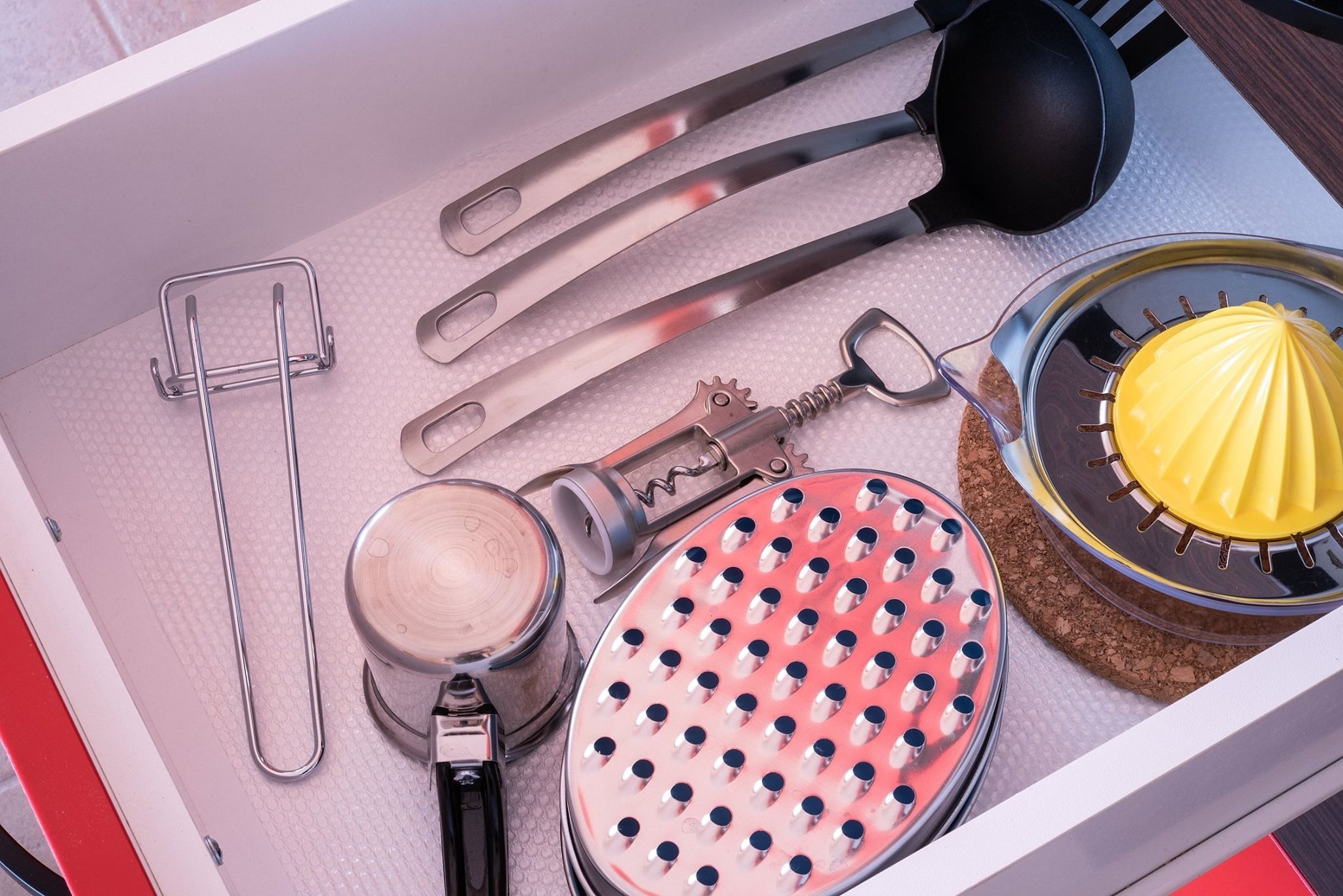 A drawer containing kitchen utensils including a grater, a can opener, a spatula, and a yellow citrus squeezer.