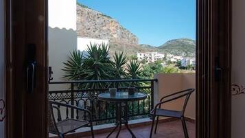 A balcony with a table and chairs, a view of a mountain, and a building in the background.