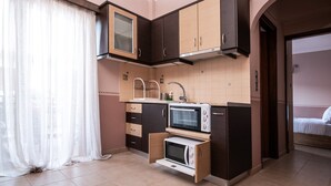 Cocina compacta con electrodomésticos integrados, una ventana con cortinas translúcidas y un lavamanos pequeño.