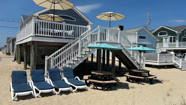 A beachfront property with a wooden deck, lounge chairs, and picnic tables.