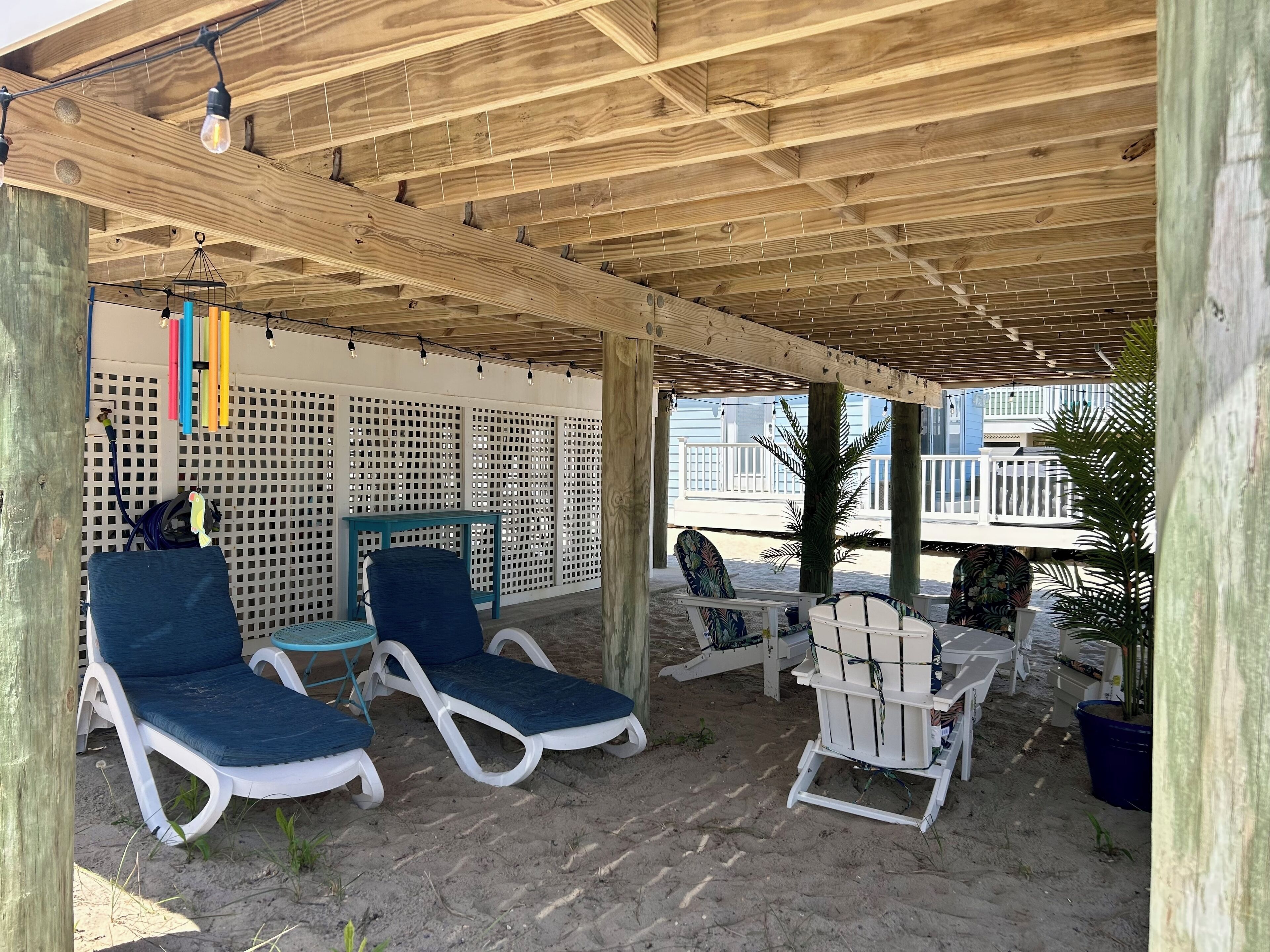 Un espace extérieur abrité, aménagé avec des fauteuils et une table, des poutres en bois au plafond et une clôture en treillis blanc.