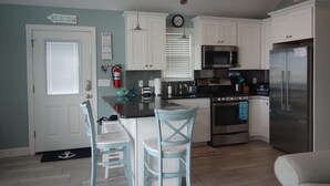 A compact kitchen with white cabinets, a stainless steel refrigerator, a microwave, and an oven. There are two light blue chairs and a small island with a sink.