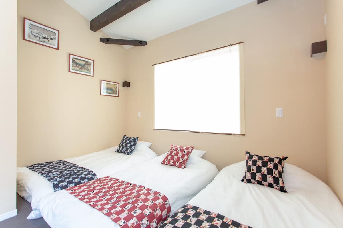 A room with two beds, each with patterned bedding, a large window, and framed pictures on the wall.