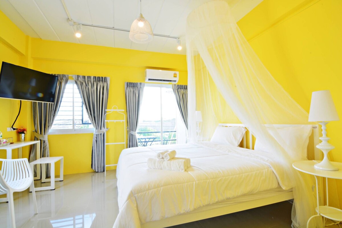 A bright yellow room with a bed, a TV, and a desk with a chair.