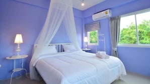 Un dormitorio con cama, ropa de cama blanca, una mesita de noche con lámpara, un aire acondicionado y una ventana con cortinas.