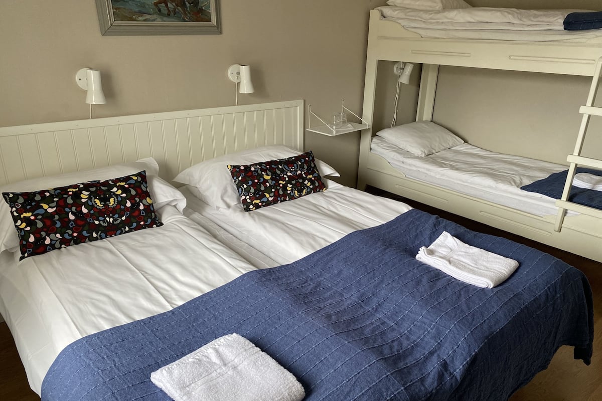 Ein Zimmer mit zwei Betten, eines mit blauer Bettdecke und weißen Handtüchern, das andere mit weißer Bettwäsche.