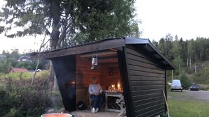 Eine kleine Holzhütte mit Veranda, Feuerstelle und Laterne über dem Eingang.