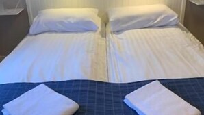 Ein Doppelbett mit weißen Laken, zwei Nachttischlampen und zwei gefaltete Handtücher auf dem Bett.