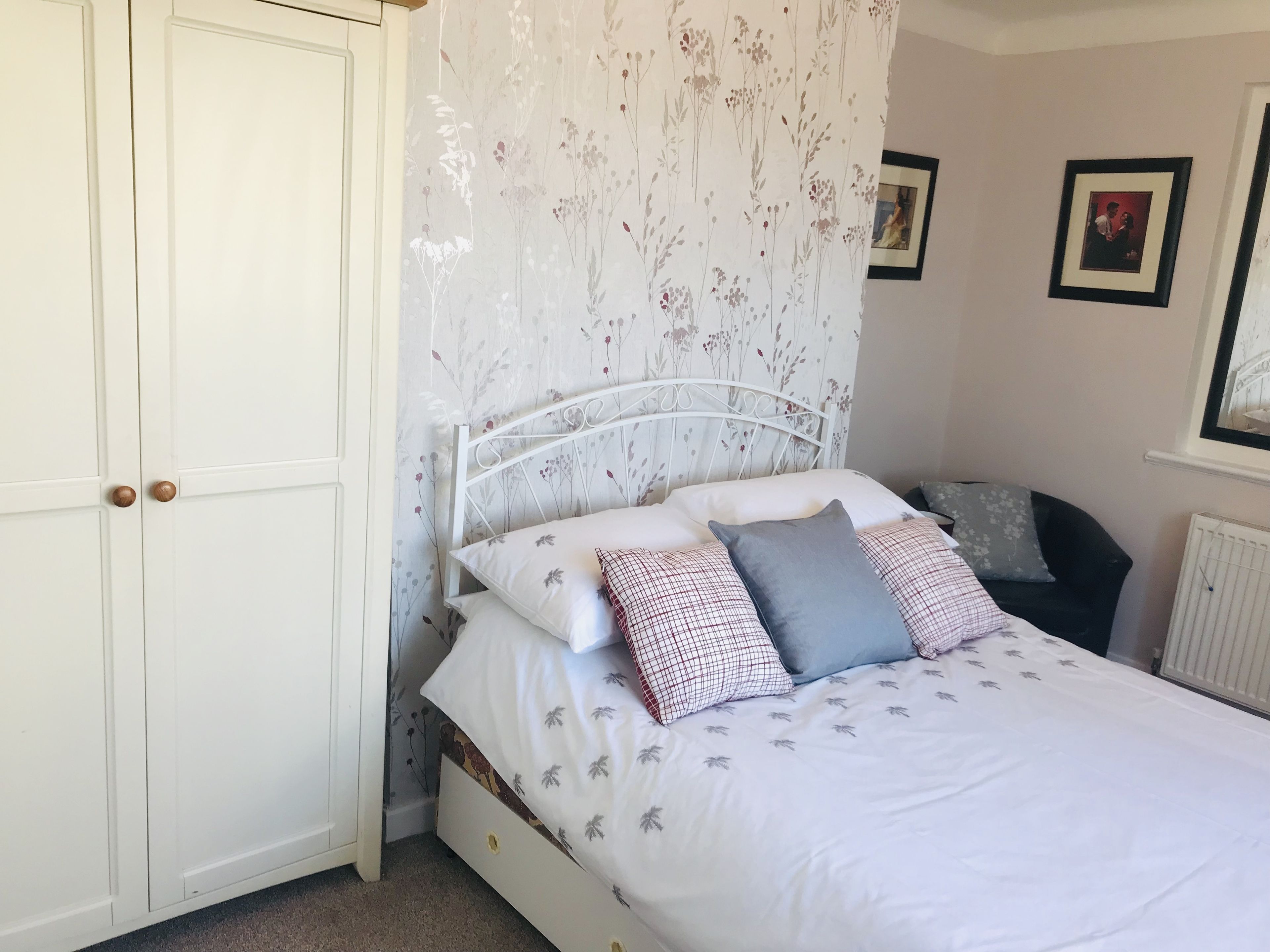 A bedroom with a white bed, floral wallpaper, and a wardrobe.