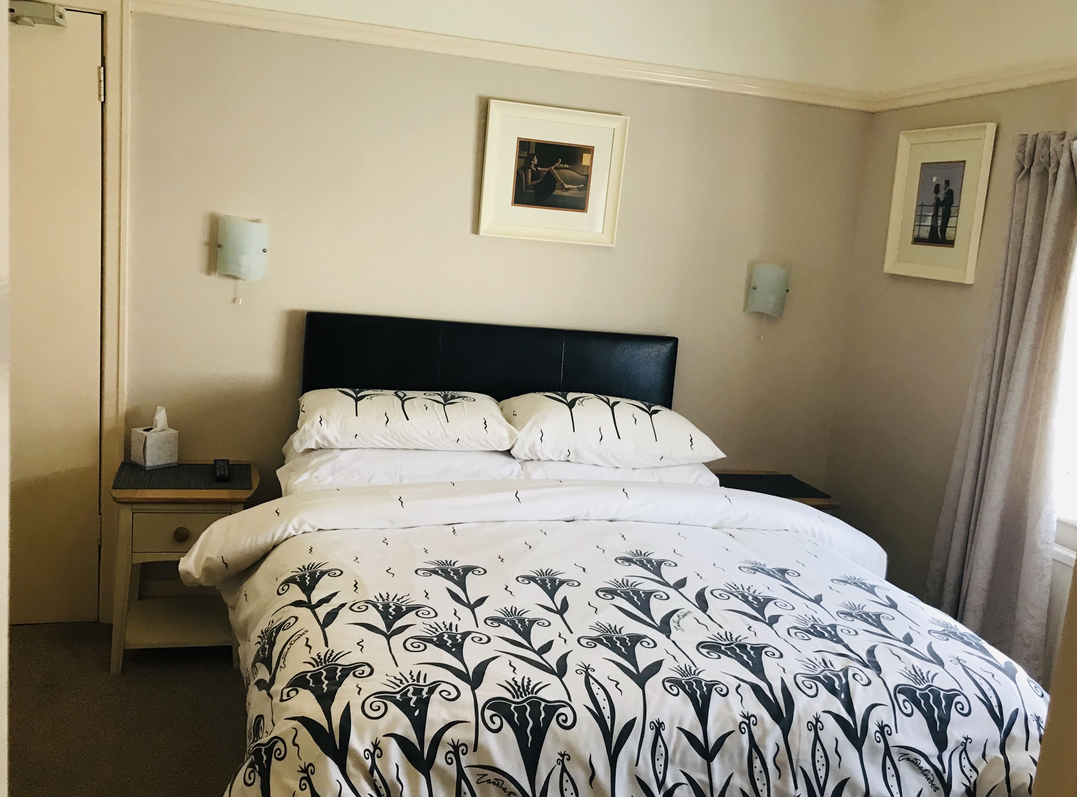 A neatly made bed with a patterned bedspread, a bedside table with a tissue box, and a framed picture on the wall.