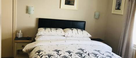A neatly made bed with a patterned bedspread, a bedside table with a tissue box, and a framed picture on the wall.