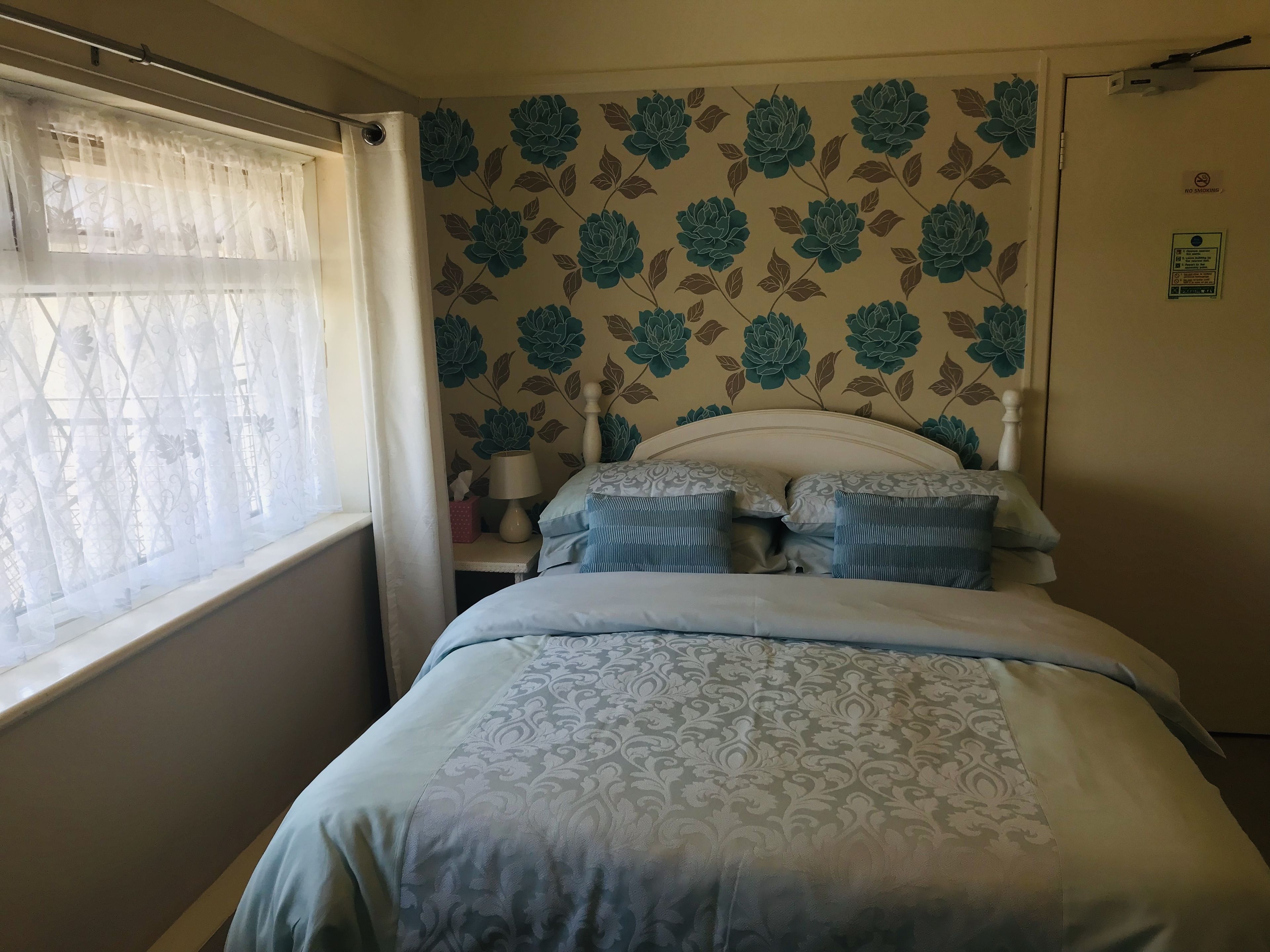 A bedroom with a bed, a nightstand, a lamp, and a window with sheer curtains.