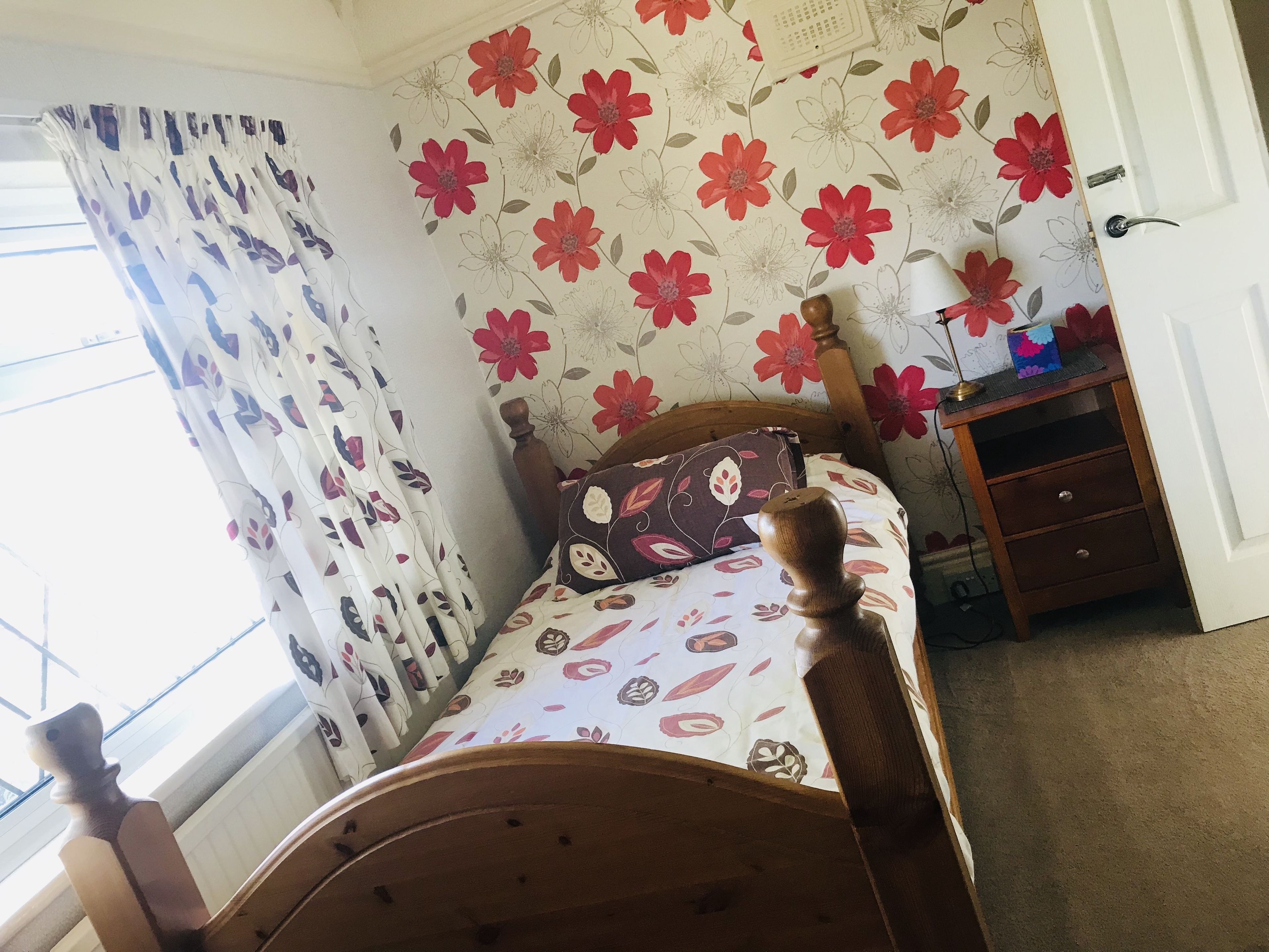 Une chambre à coucher avec un lit, une tête de lit en bois, une table de chevet avec une lampe, une commode et une fenêtre avec des rideaux.